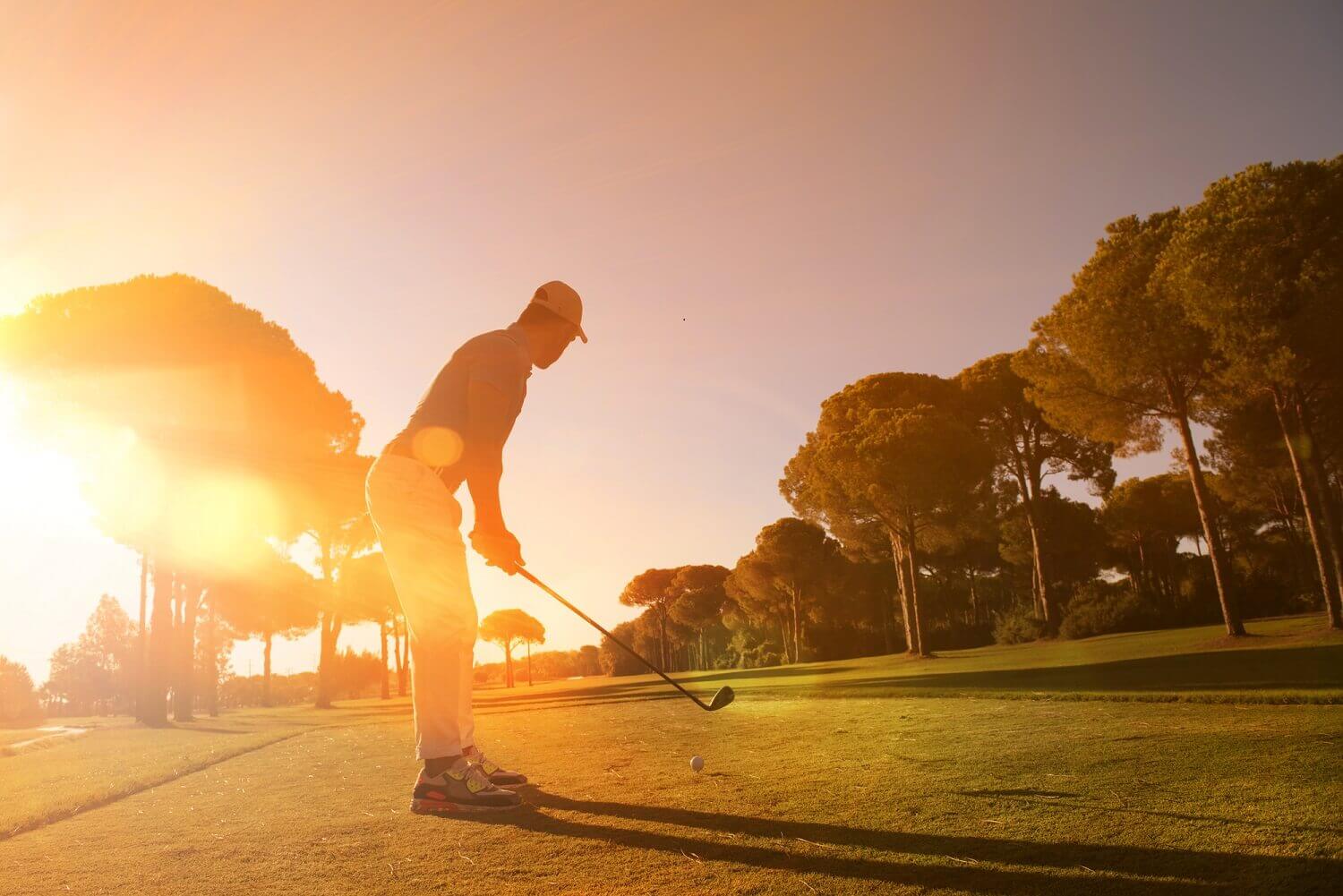 man playing golf with sunset in background